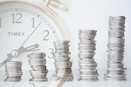stacks of coins increasing in size with a clock in the background